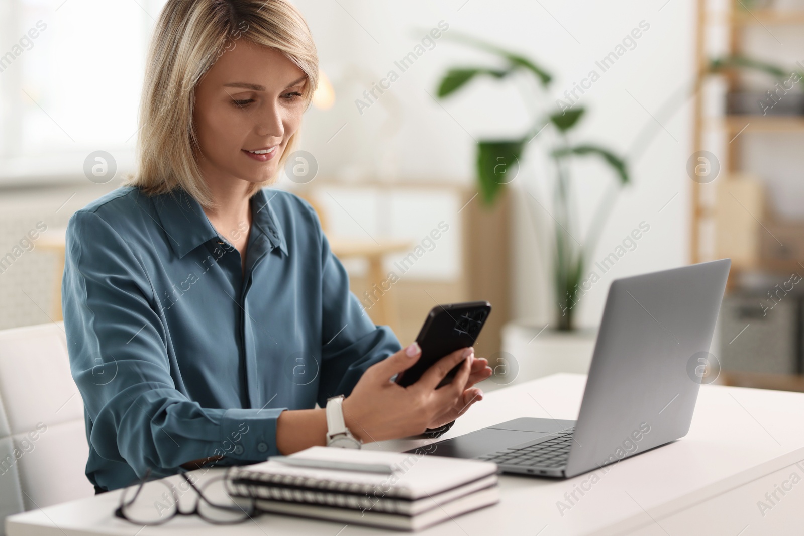 Photo of Happy woman using mobile phone at white table indoors