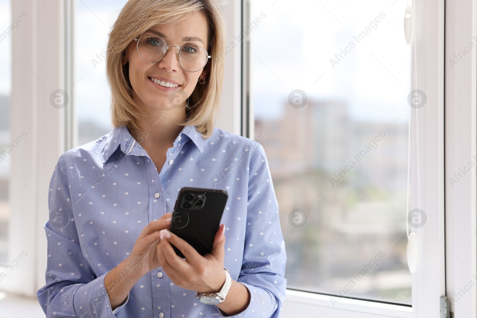 Photo of Happy woman using mobile phone near window indoors, space for text