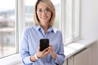 Happy woman using mobile phone near window indoors