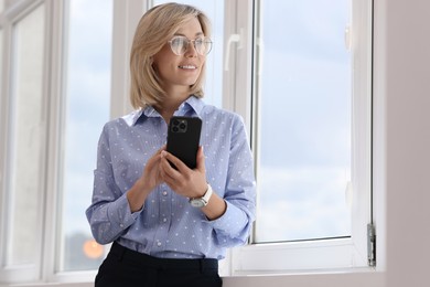 Happy woman using mobile phone near window indoors, space for text