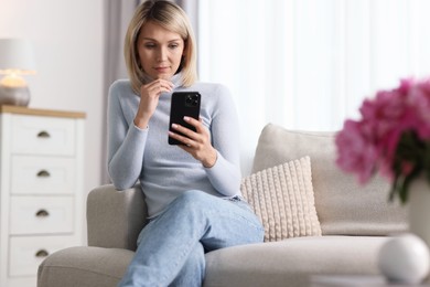 Woman using mobile phone on sofa at home