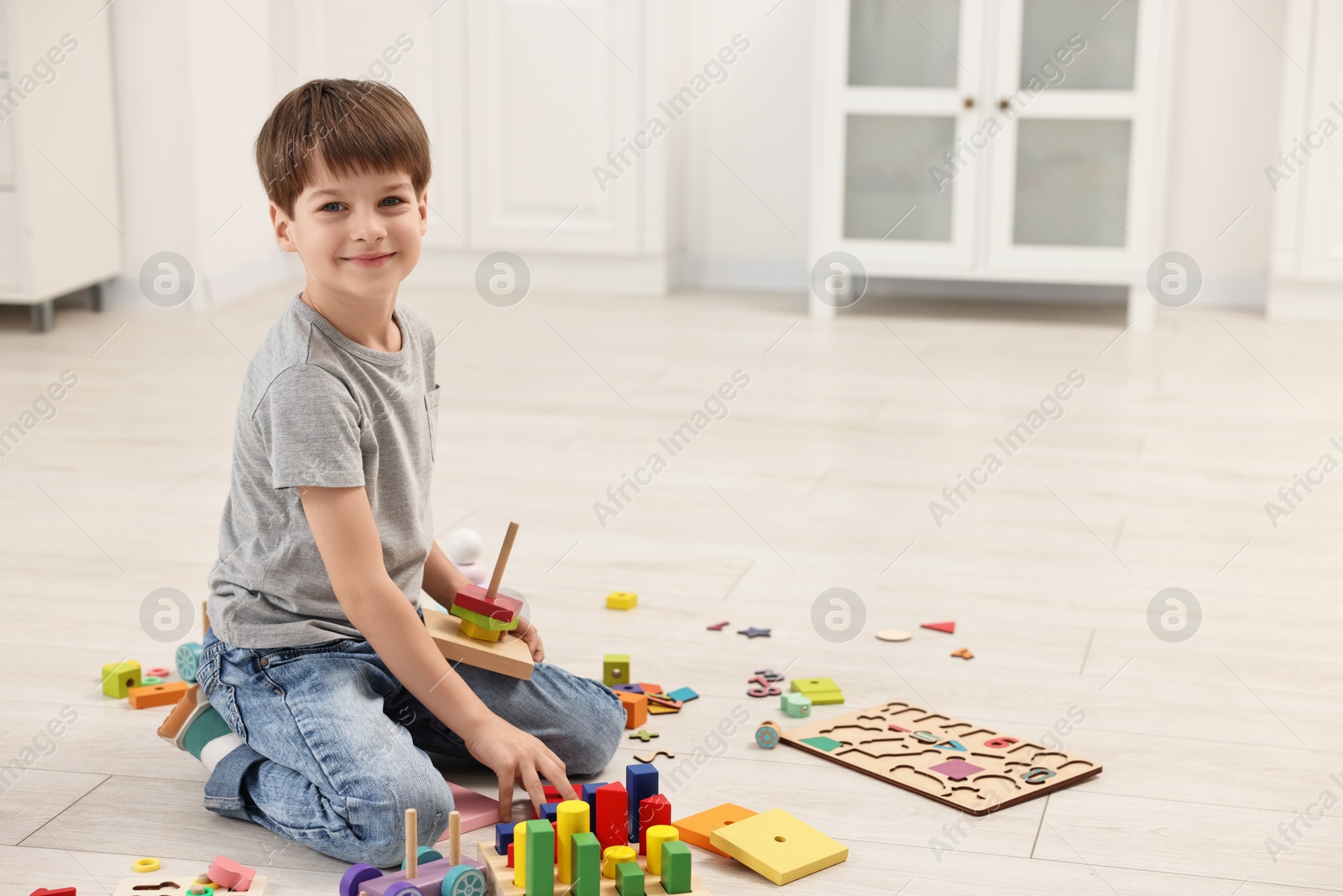 Photo of Cute little boy playing with toy pyramid on floor indoors