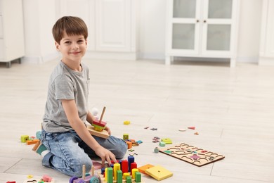 Cute little boy playing with toy pyramid on floor indoors