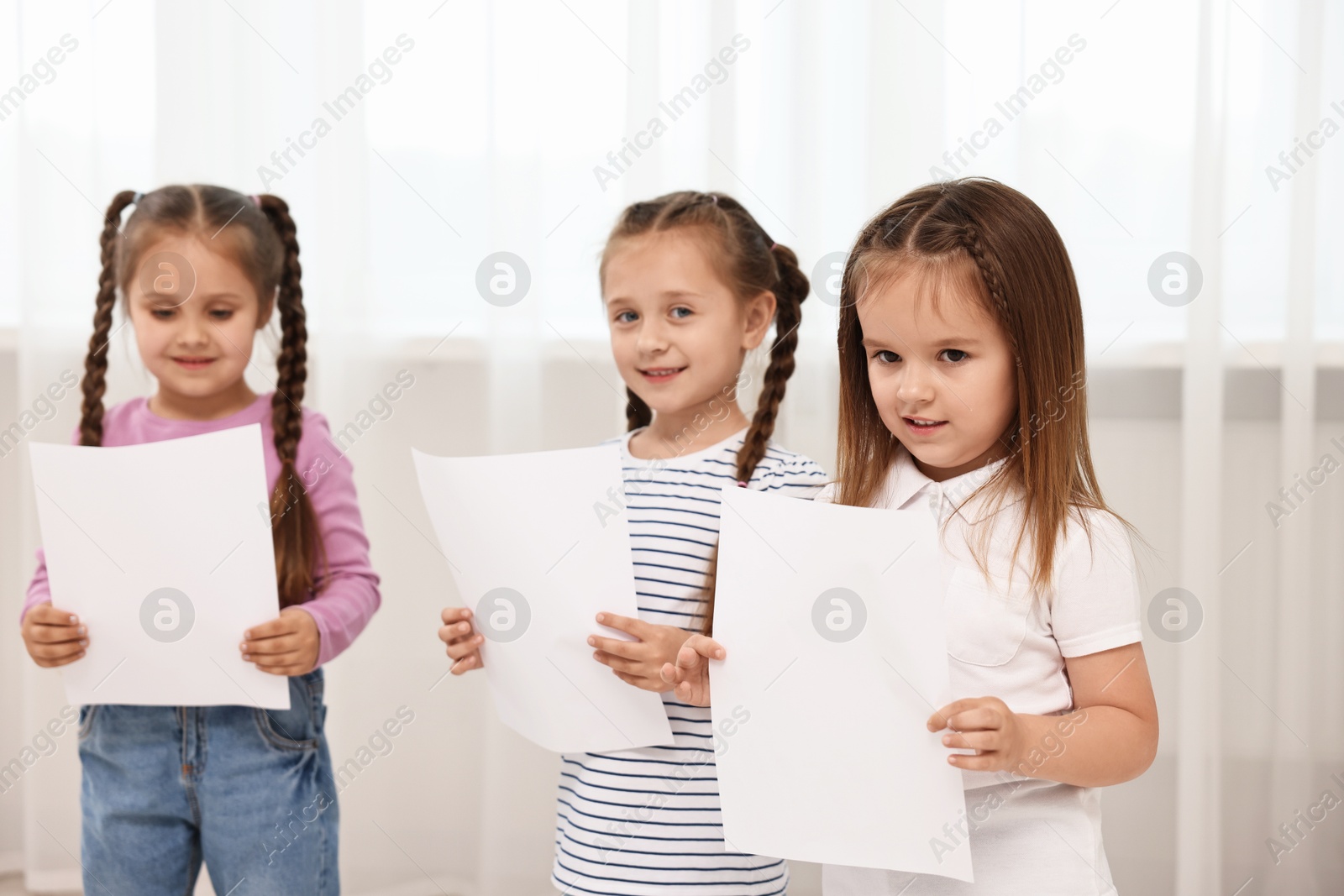 Photo of Cute little children with sheets of paper singing indoors