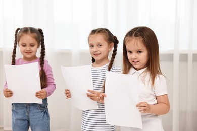 Photo of Cute little children with sheets of paper singing indoors