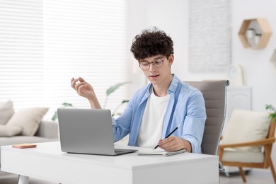 Teenager taking notes while working with laptop on sofa at home. Remote job