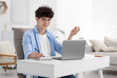 Teenager taking notes while working with laptop on sofa at home. Remote job