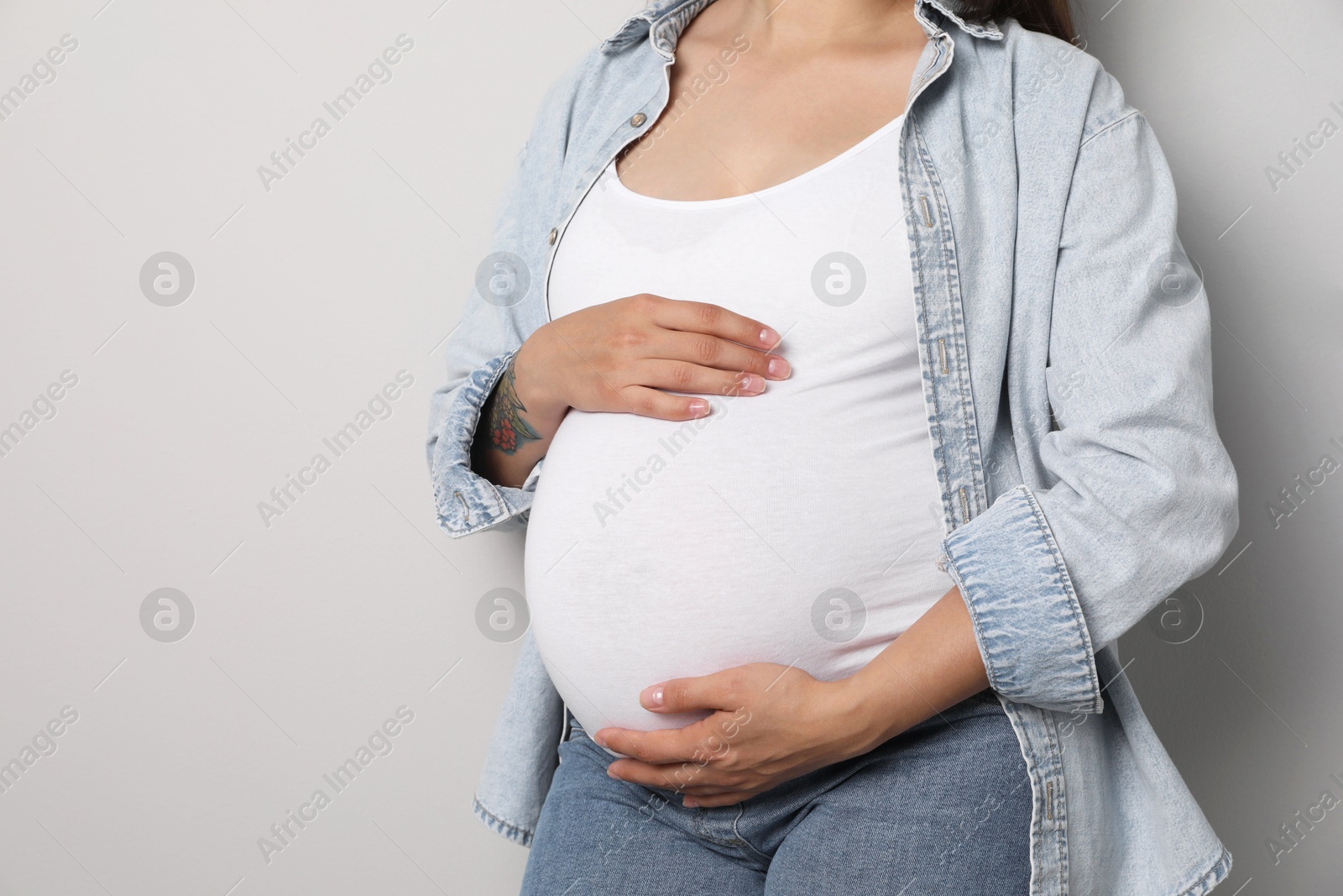 Photo of Pregnant woman on gray background, closeup. Space for text