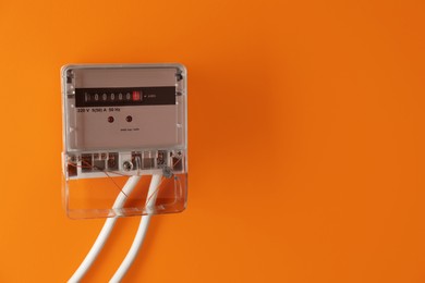 Photo of Electric meter on orange background, space for text. Energy measuring device