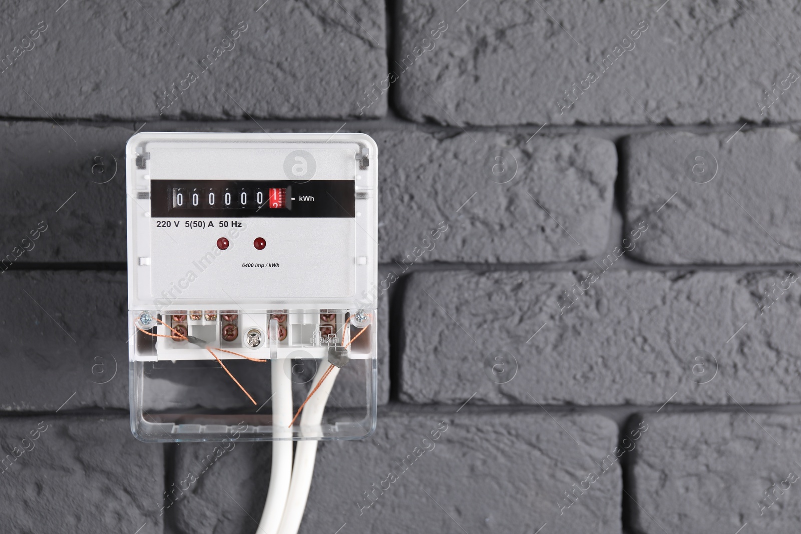 Photo of Electric meter on grey brick wall, space for text. Energy measuring device