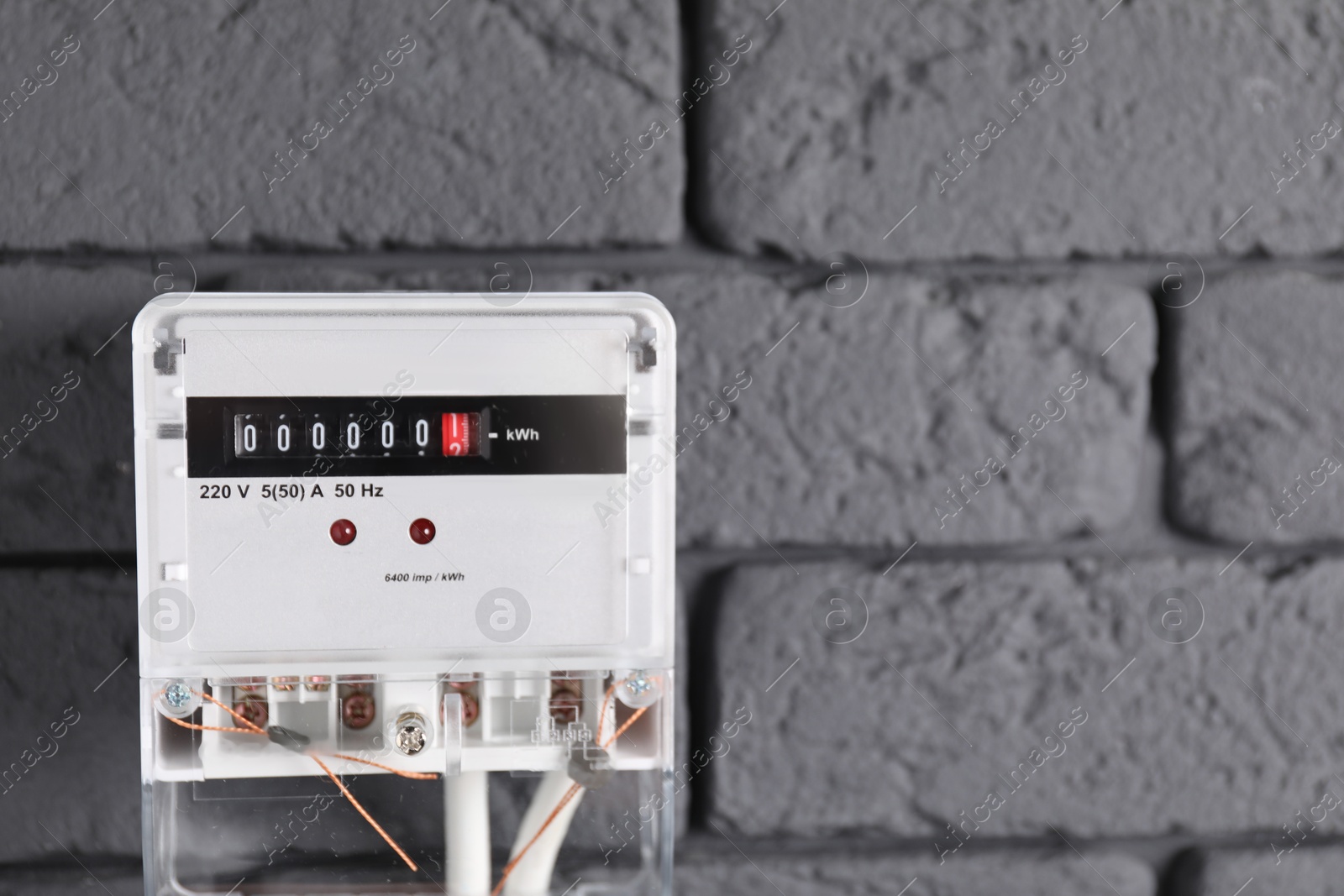 Photo of Electric meter on grey brick wall, space for text. Energy measuring device