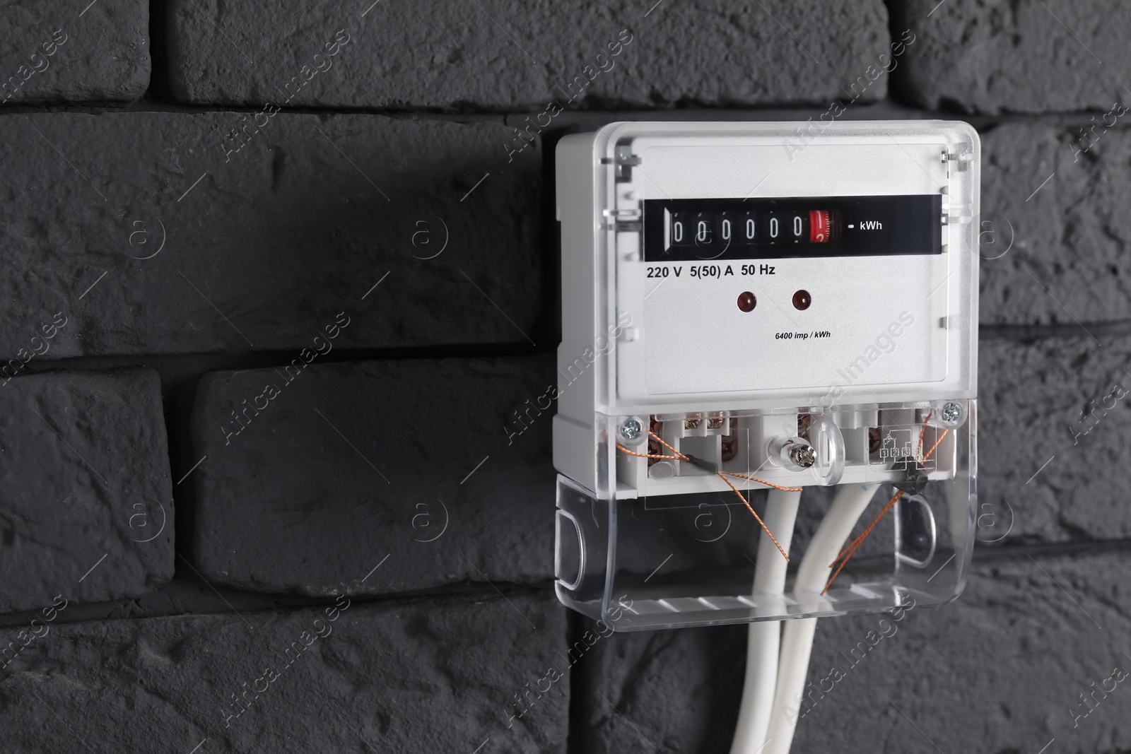 Photo of Electric meter on grey brick wall, space for text. Energy measuring device