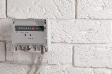 Photo of Electric meter on white brick wall, space for text. Energy measuring device