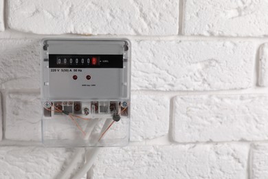 Photo of Electric meter on white brick wall, space for text. Energy measuring device