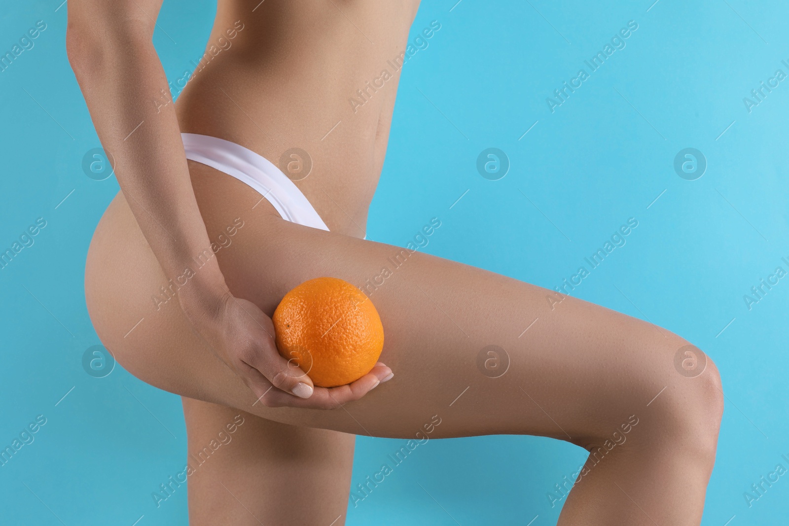 Photo of Woman in underwear with orange on light blue background, closeup. Cellulite problem