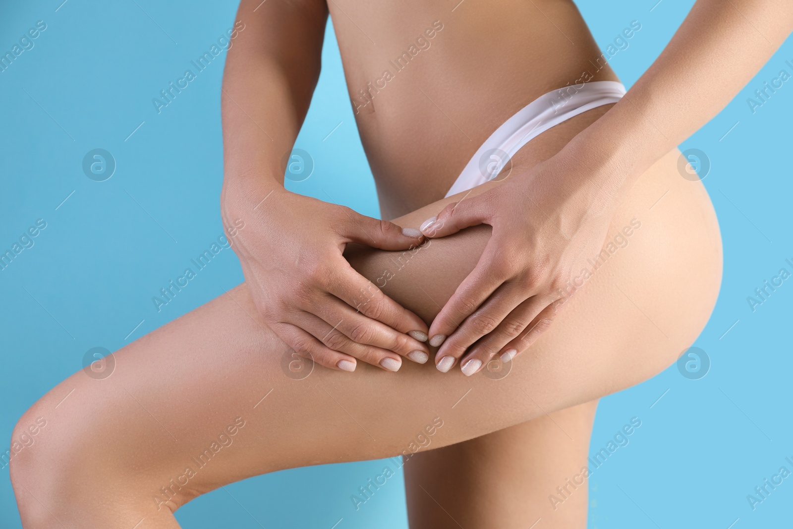 Photo of Woman in underwear making heart with hands near thigh on light blue background, closeup. Cellulite problem