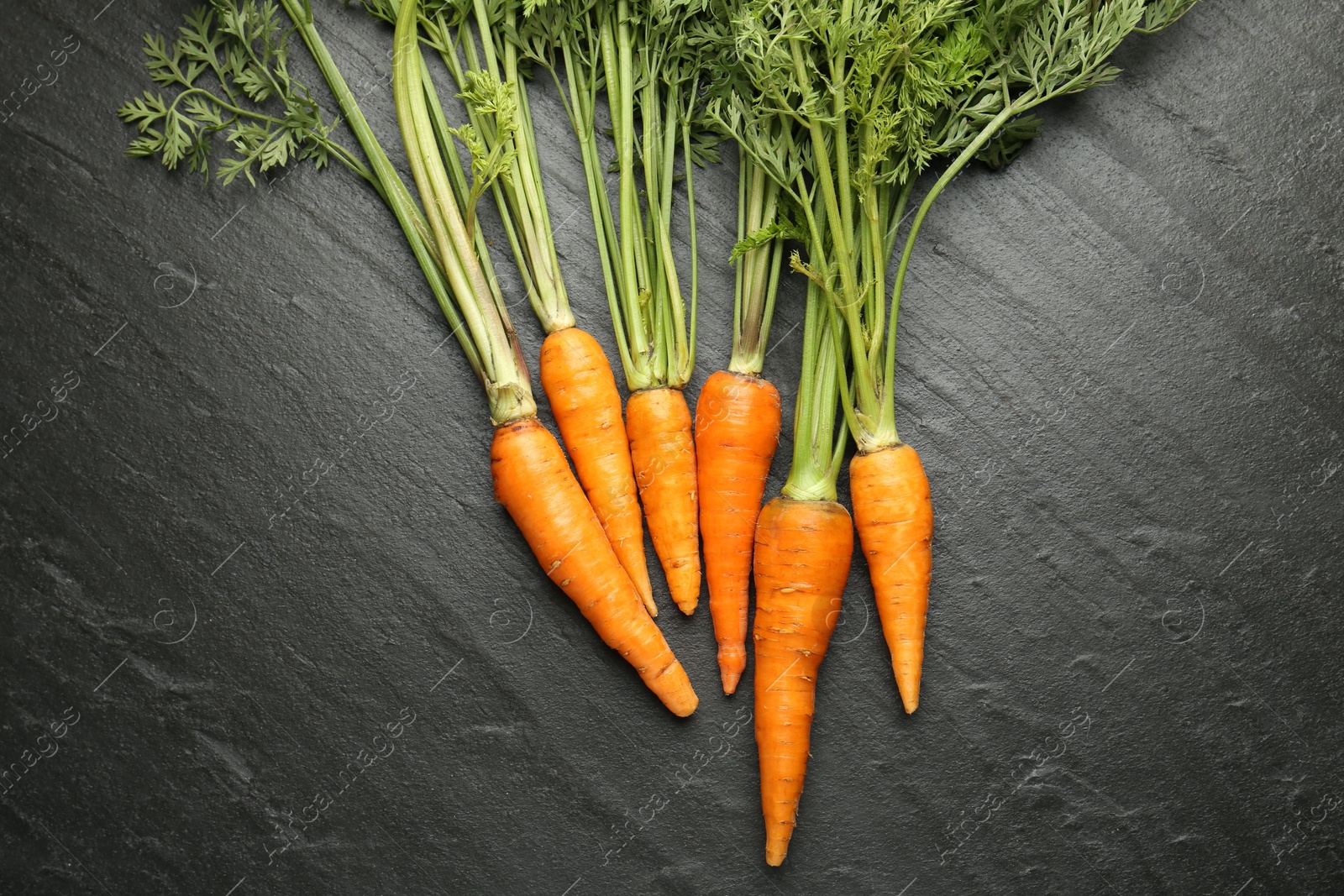 Photo of Tasty ripe juicy carrots on dark gray textured table, top view