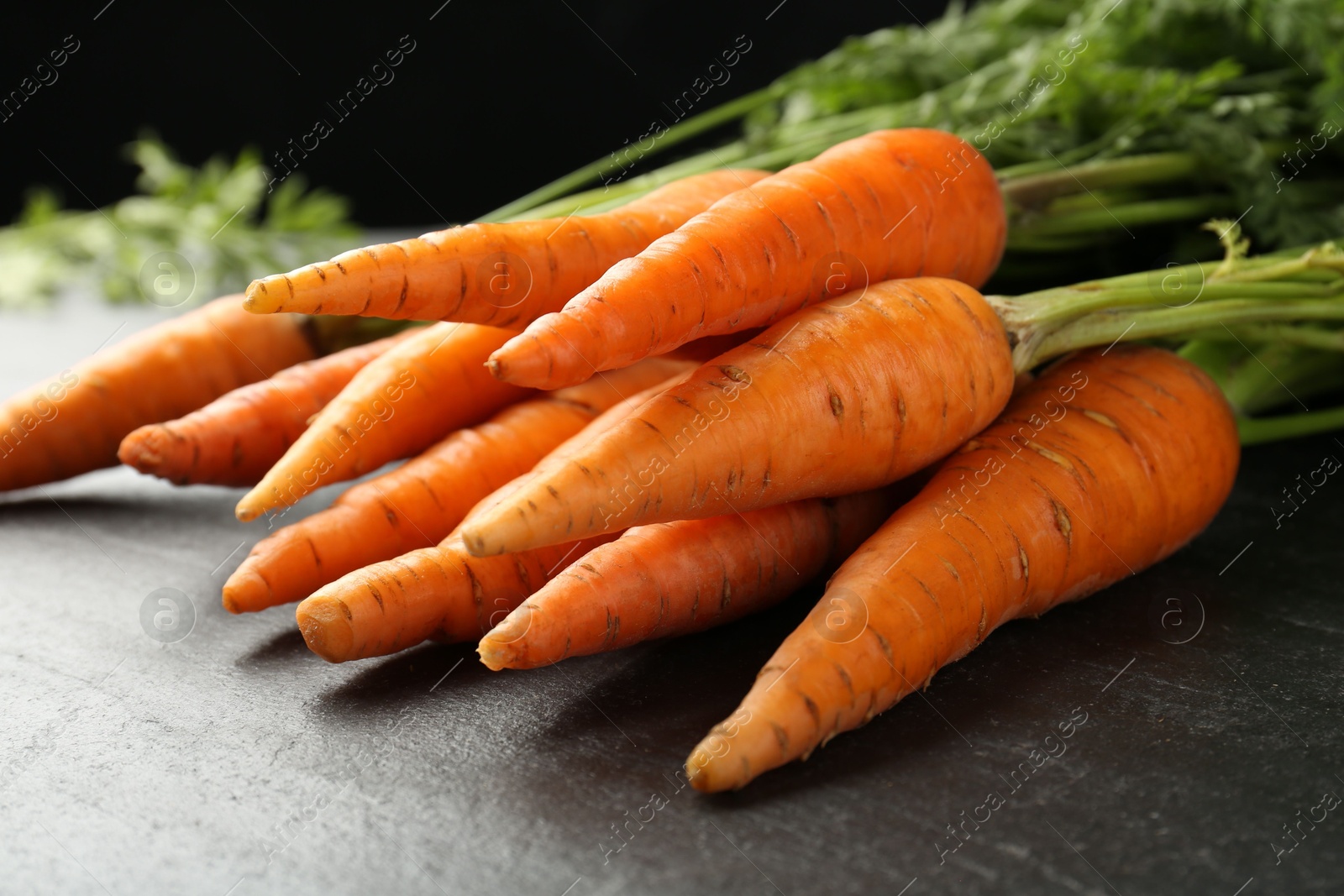 Photo of Tasty ripe juicy carrots on dark gray textured table, closeup