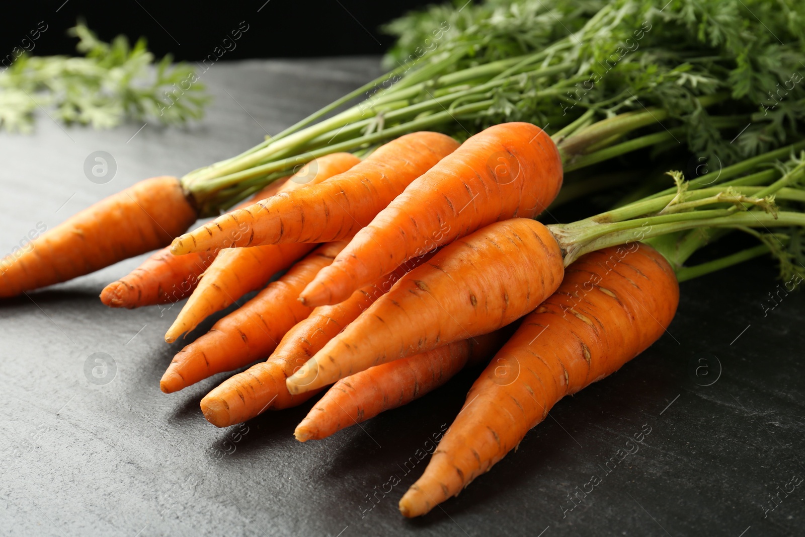 Photo of Tasty ripe juicy carrots on dark gray textured table, closeup