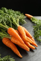 Photo of Tasty ripe juicy carrots on dark gray textured table, closeup