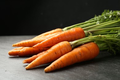 Photo of Tasty ripe juicy carrots on dark gray textured table, closeup