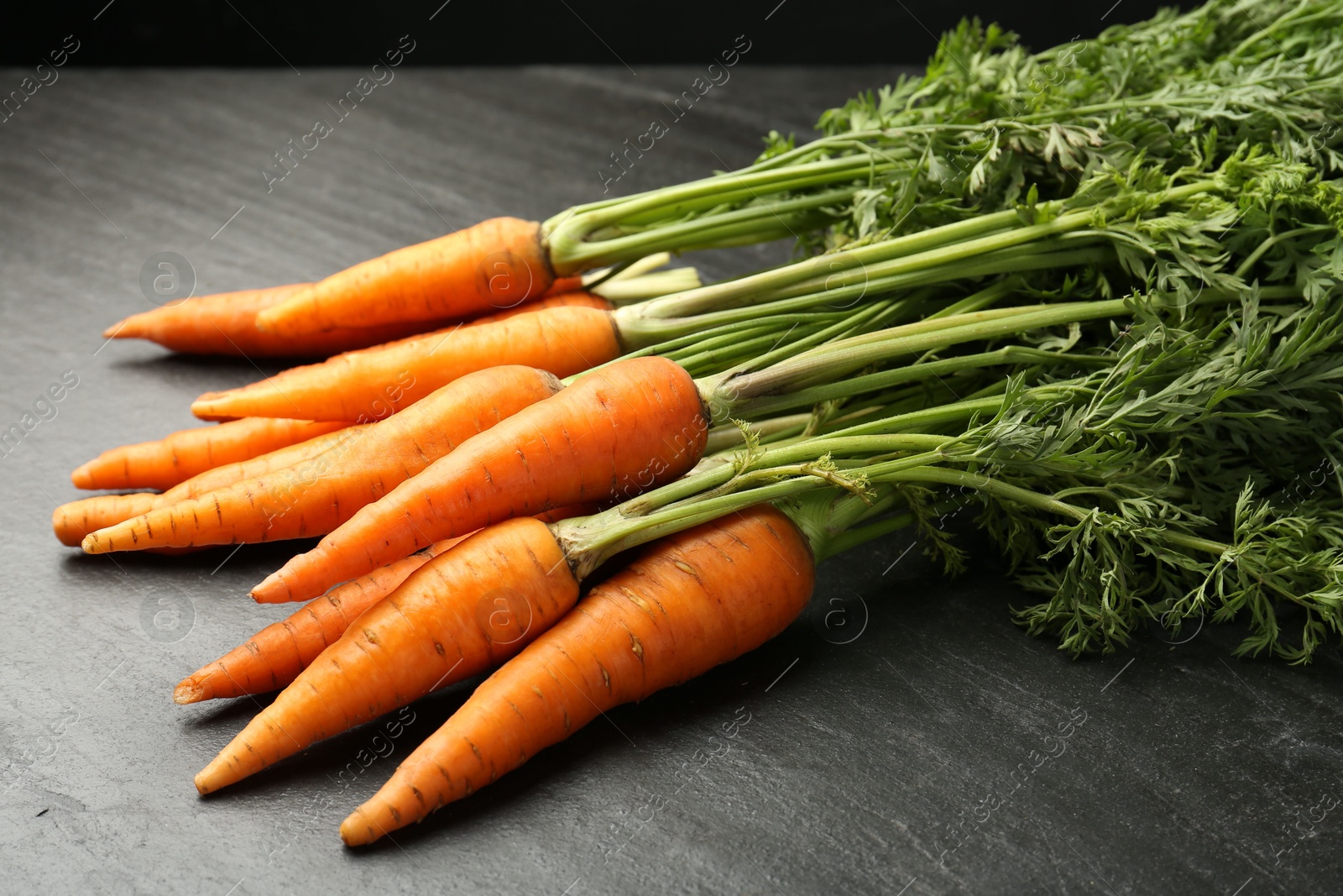 Photo of Tasty ripe juicy carrots on dark gray textured table, closeup