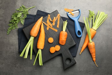 Photo of Fresh carrots, vegetable peeler and peels on gray textured table, flat lay