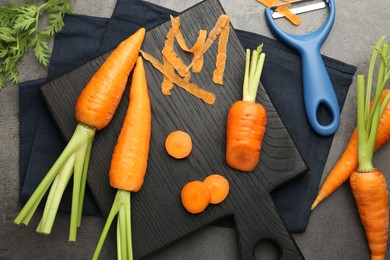 Photo of Fresh carrots, vegetable peeler and peels on gray textured table, flat lay