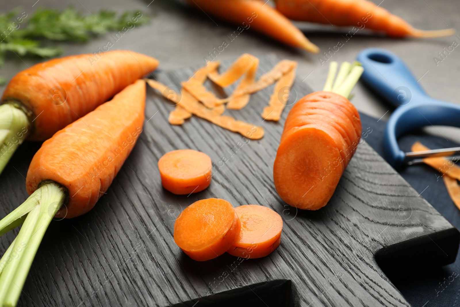 Photo of Fresh carrots, vegetable peeler and peels on gray table, closeup