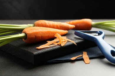 Photo of Fresh carrots, vegetable peeler and peels on gray textured table, closeup