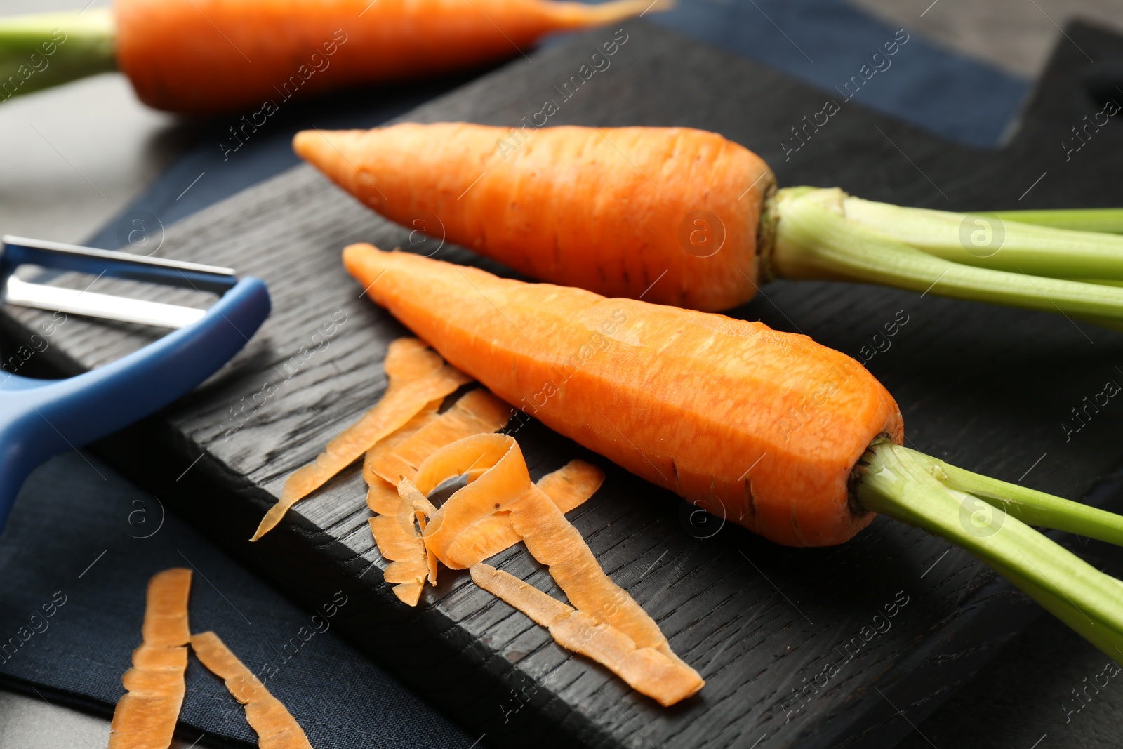 Photo of Fresh carrots, vegetable peeler and peels on table, closeup