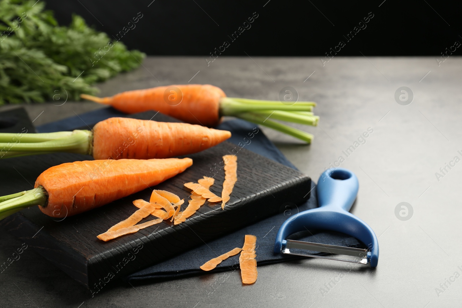 Photo of Fresh carrots, vegetable peeler and peels on gray textured table, closeup