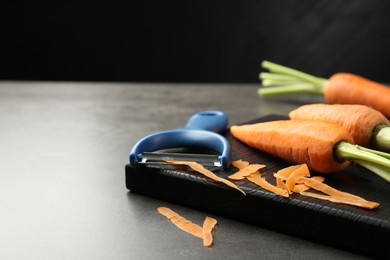 Photo of Fresh carrots, vegetable peeler and peels on gray textured table, closeup. Space for text