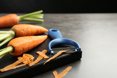 Photo of Fresh carrots, vegetable peeler and peels on gray textured table, closeup. Space for text