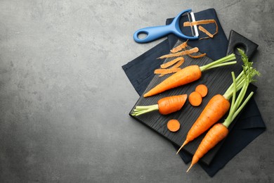 Fresh carrots, vegetable peeler and peels on gray textured table, flat lay. Space for text