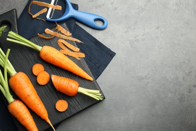 Fresh carrots, vegetable peeler and peels on gray textured table, flat lay. Space for text