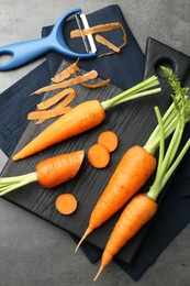 Photo of Fresh carrots, vegetable peeler and peels on gray textured table, flat lay