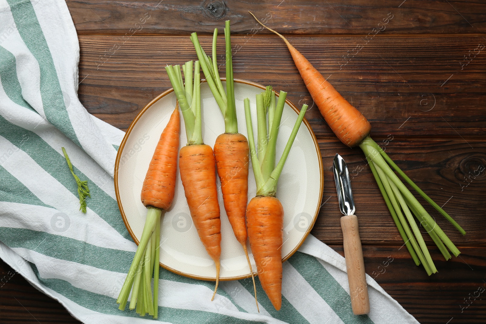 Photo of Fresh carrots and vegetable peeler on wooden table, flat lay