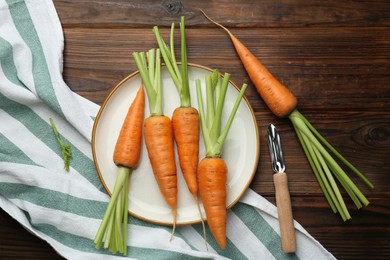 Fresh carrots and vegetable peeler on wooden table, flat lay