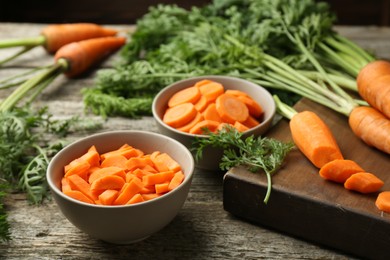 Photo of Cut carrots in bowls on wooden table, closeup