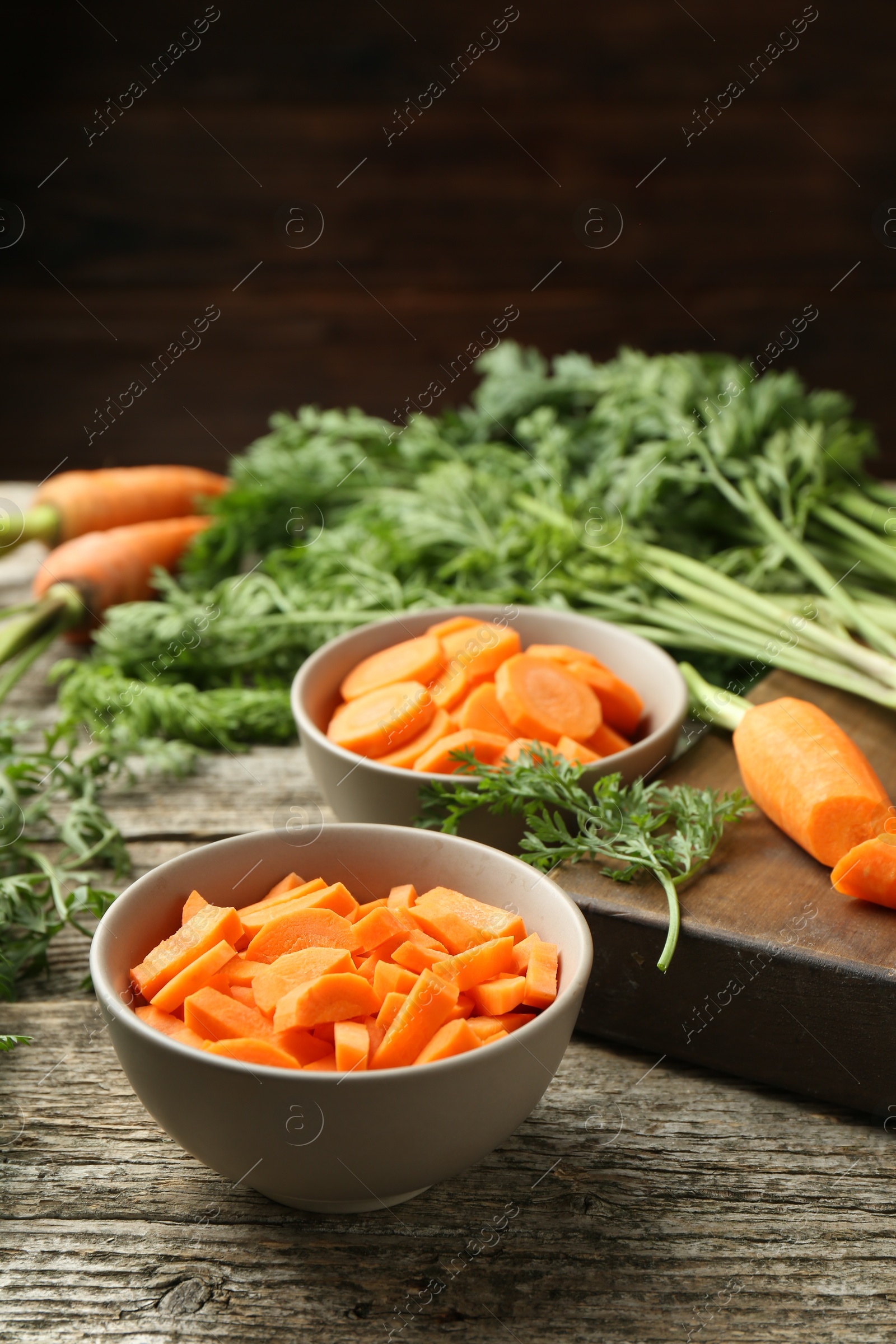 Photo of Cut carrots in bowls on wooden table, closeup