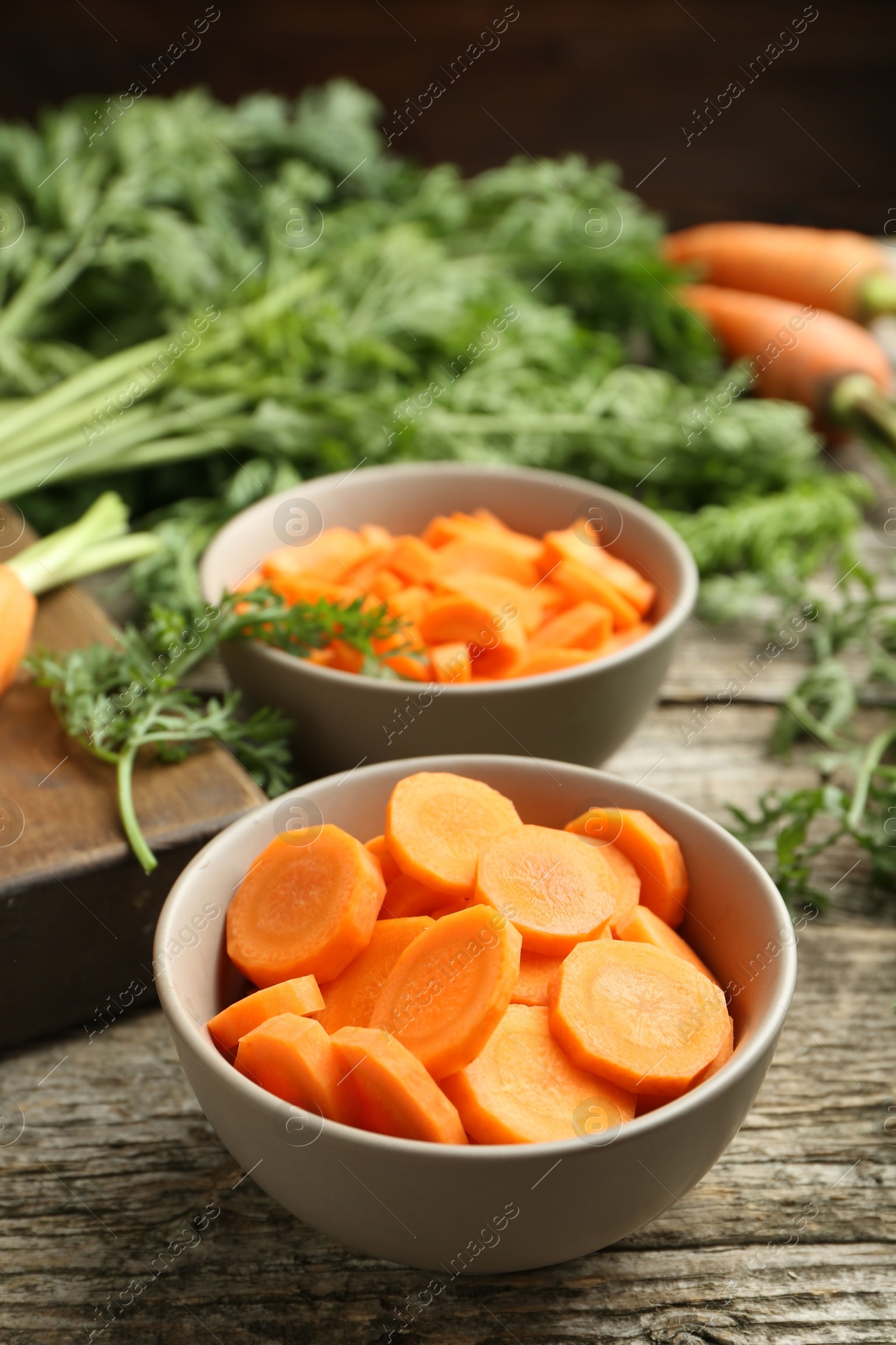 Photo of Cut carrots in bowls on wooden table, closeup