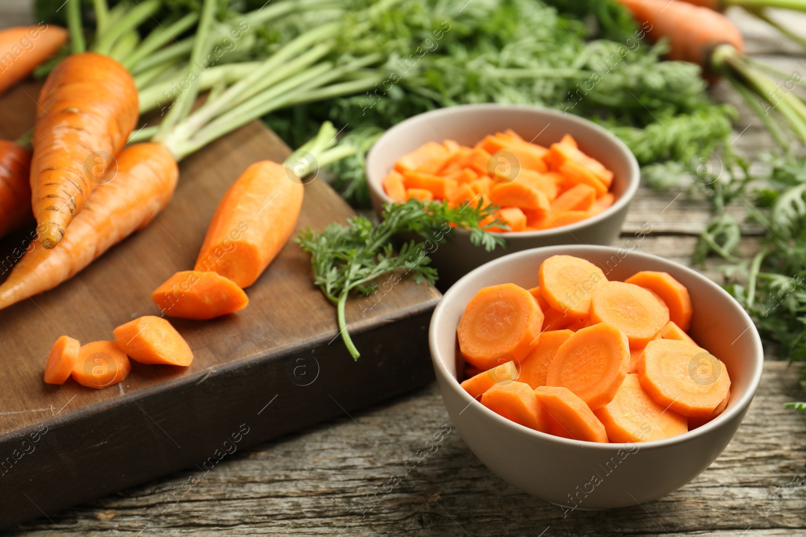 Photo of Cut carrots in bowls on wooden table, closeup