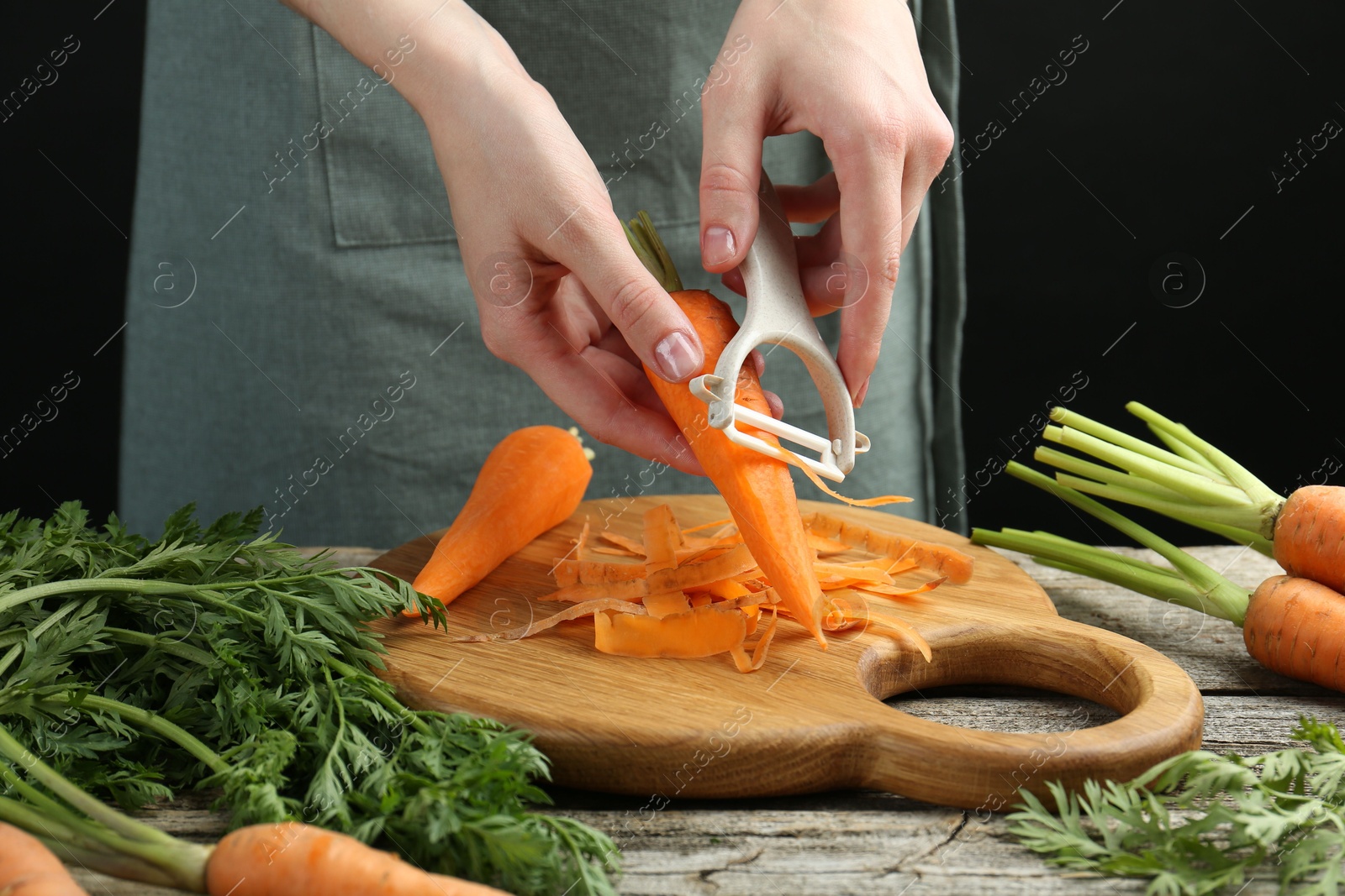 Photo of Woman peeling fresh carrot at wooden table, closeup