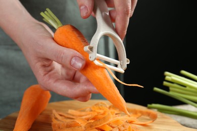 Photo of Woman peeling fresh carrot at wooden table, closeup