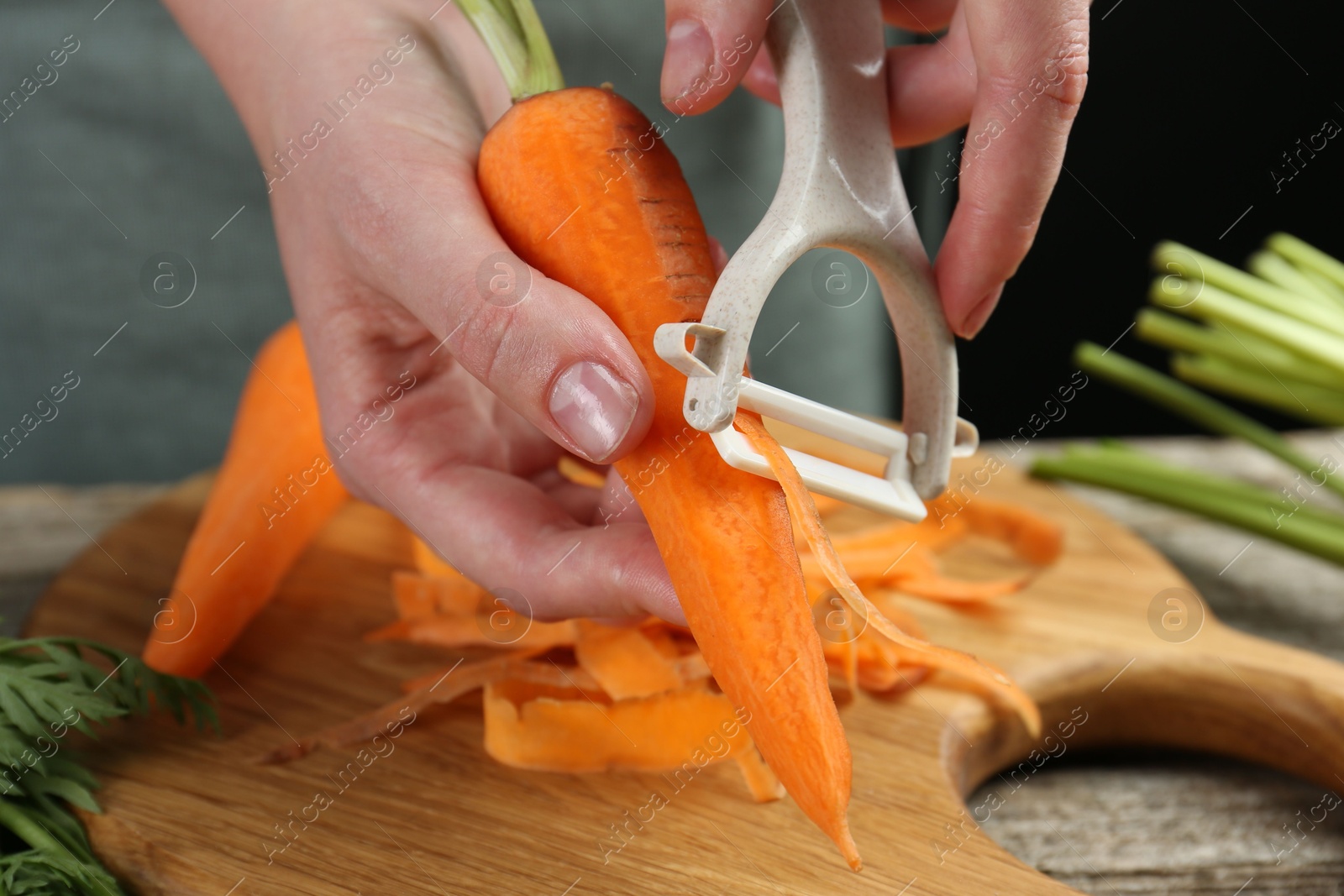 Photo of Woman peeling fresh carrot at wooden table, closeup