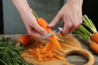 Photo of Woman peeling fresh carrot with knife at wooden table, closeup