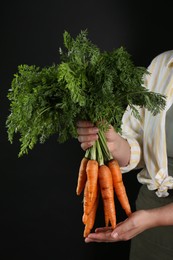 Photo of Woman holding ripe carrots on black background, closeup