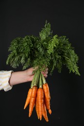 Photo of Woman holding ripe carrots on black background, closeup