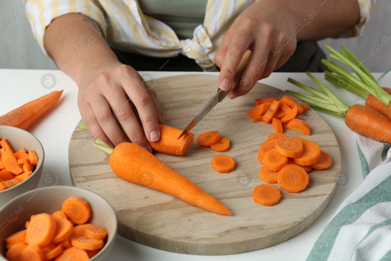 Photo of Woman cutting fresh carrot at white table, closeup